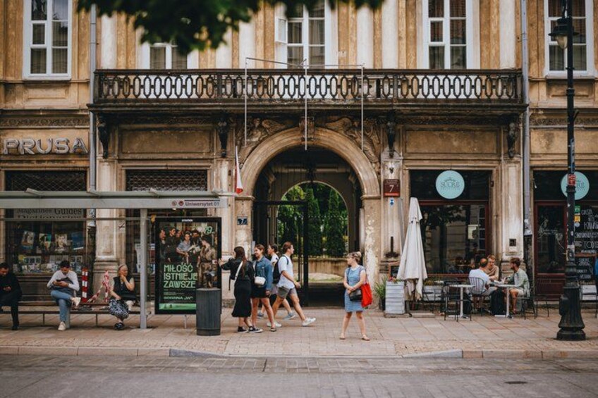 A historic building with an ornate archway, a cafe with outdoor seating, and a pedestrian walkway. 3