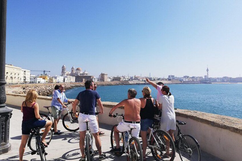 A group of people on bicycles by a waterfront, with buildings and a tower in the background. 2