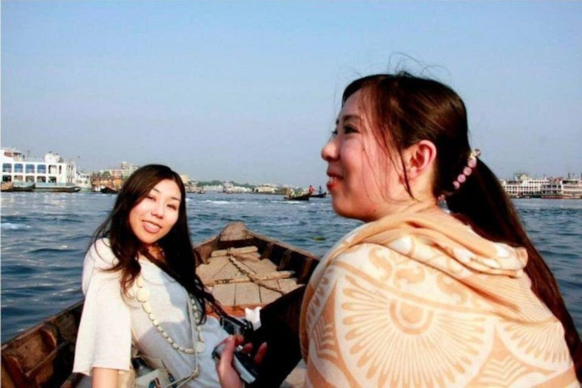 Two people on a boat with a river and buildings in the background. 2
