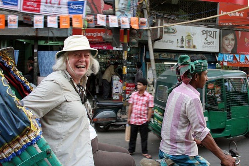Straatbeeld met een persoon in een witte hoed, een man op een motor en een groene tuk-tuk. 1