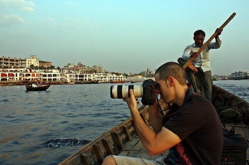 Iemand maakt een foto met een camera, een andere persoon roeit een boot, en een stadsgezicht op de achtergrond. 4