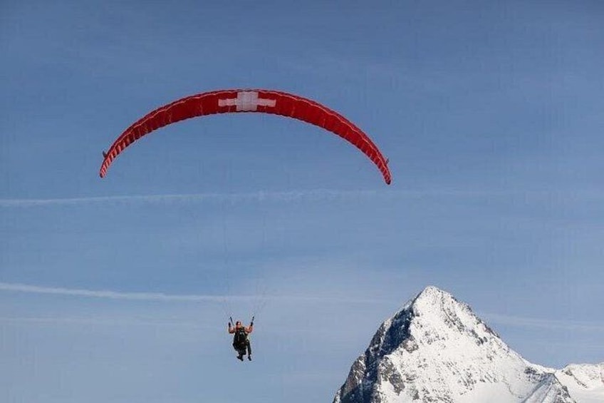 Una persona haciendo parapente con un paracaídas rojo sobre una montaña nevada. 2
