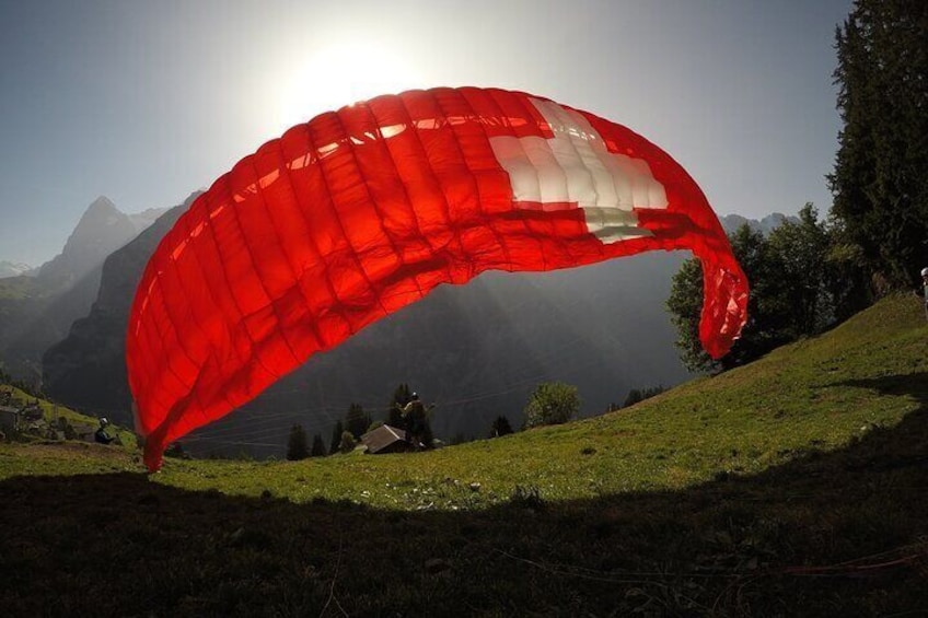 A paraglider with a red and white parachute over a grassy hill with mountains in the background. 2