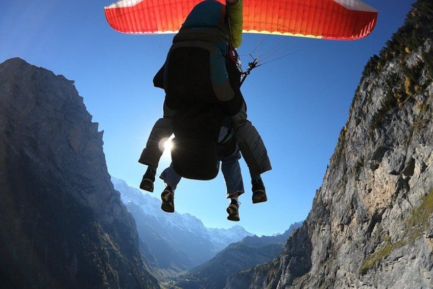 A person paragliding over a mountainous landscape with steep cliffs and distant snow-capped peaks. 2