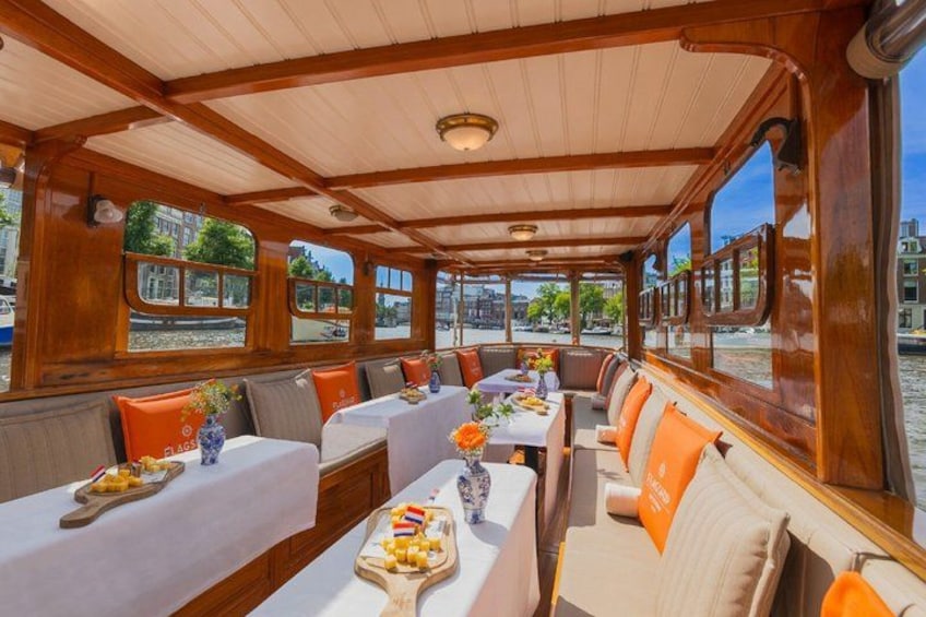 A boat interior with wooden beams, tables with white tablecloths, and orange cushions. 1