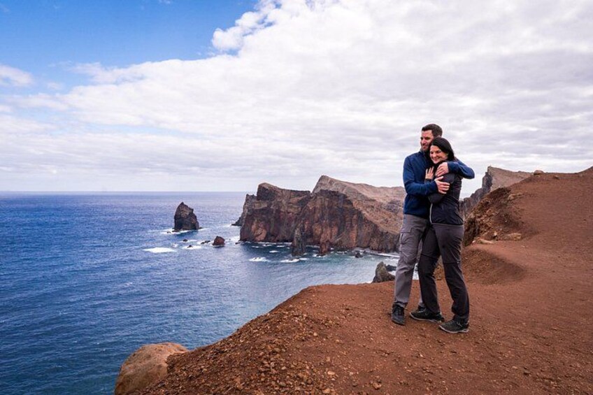 A couple embracing on a rocky cliff overlooking the ocean with cliffs in the background. 2