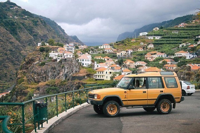 Un SUV amarillo estacionado en una carretera, con un pueblo montañoso al fondo. 1