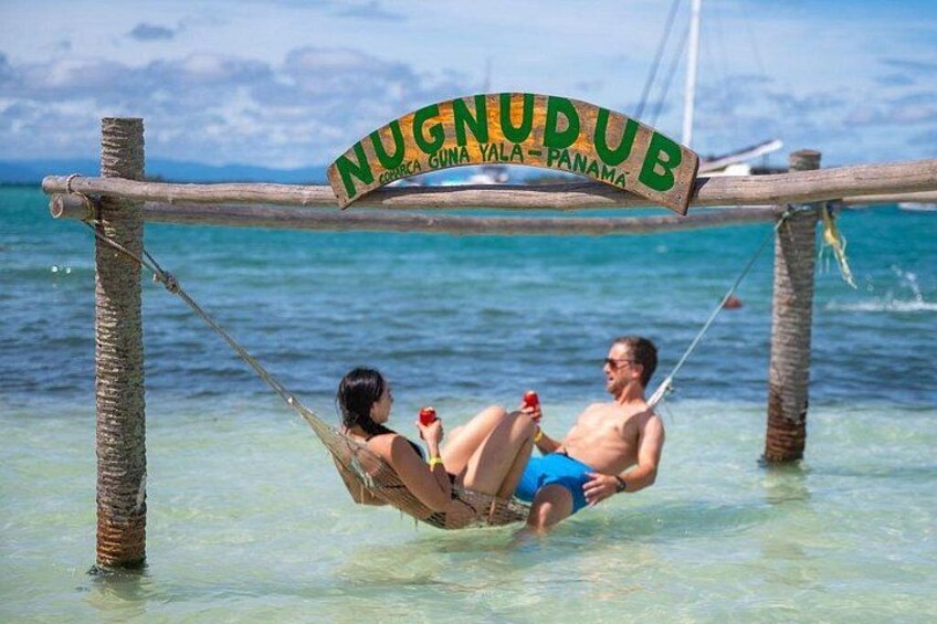 Een hangmat met een bord waarop 'NUNUDUB' staat, in een tropische omgeving. 2