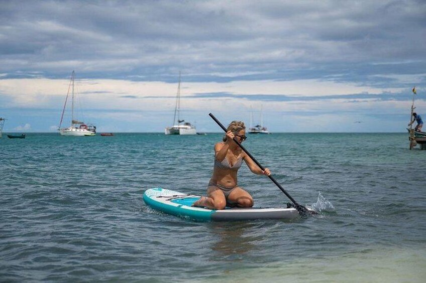 A person paddleboarding on calm water with sailboats in the background. 2