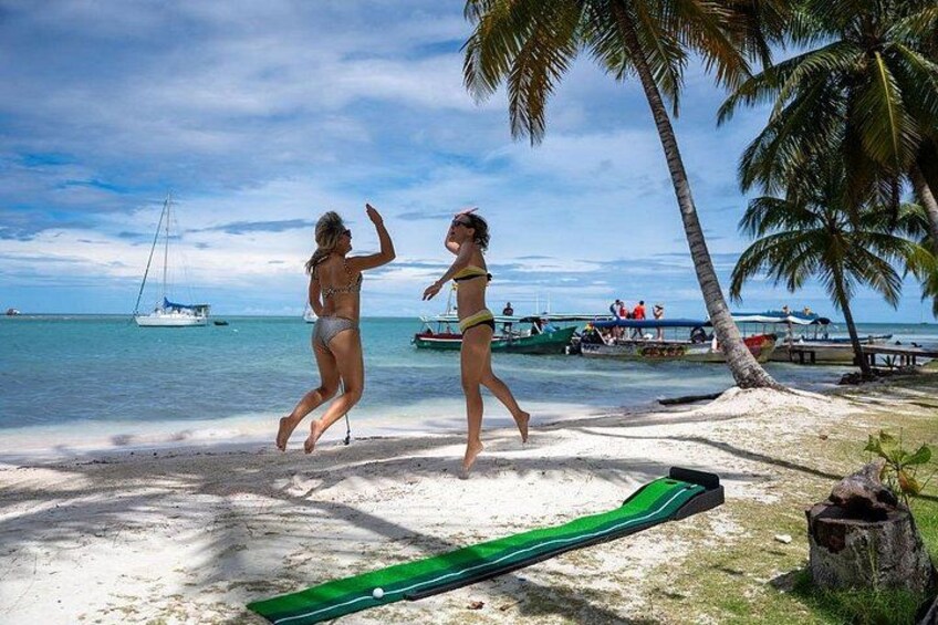 A beach with palm trees, a sailboat, and people in bikinis. 3