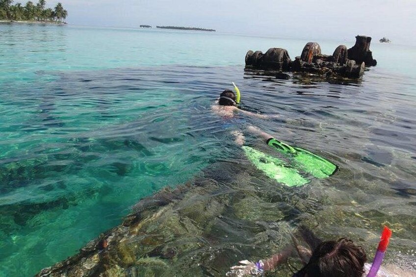 A person snorkeling in clear turquoise water with a green fin and a snorkel. 2