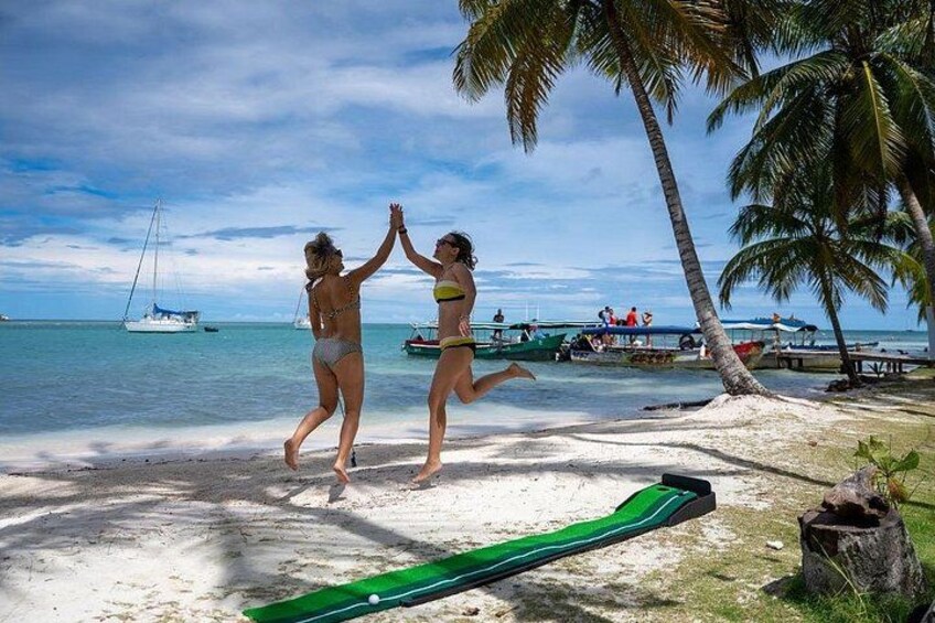 Two people dancing on a beach with palm trees, a boat, and a green slide in the foreground. 4