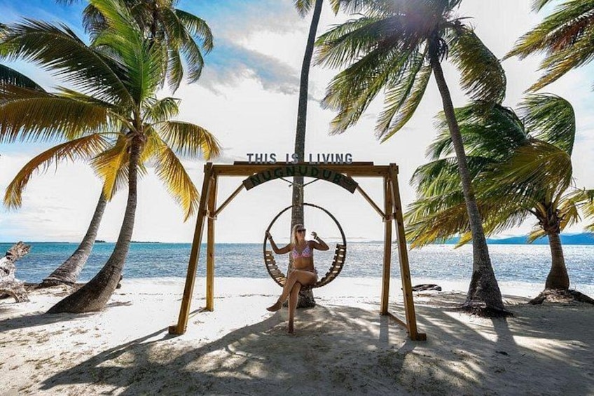 A beach with a swing set and a sign that reads 'THIS IS LIVING.' 5