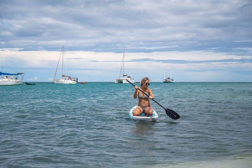 A person paddleboarding on calm waters with sailboats in the background. 3