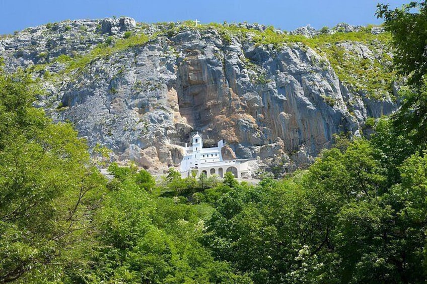 A white church nestled against a rocky cliff with lush greenery in the foreground. 2
