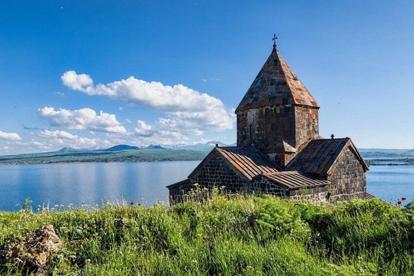 Una iglesia con un campanario junto a un lago, con montañas al fondo. 1