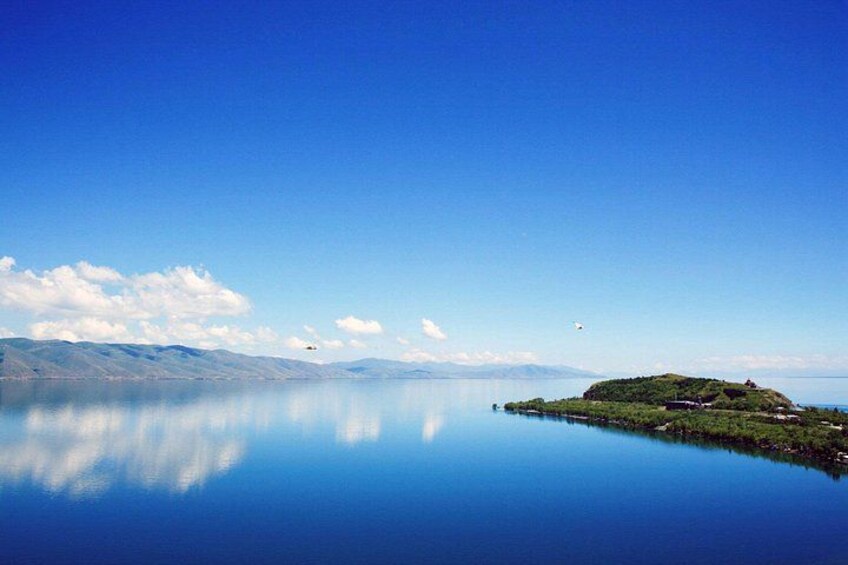 Un lago tranquilo con una pequeña isla, cielo despejado y montañas distantes. 5
