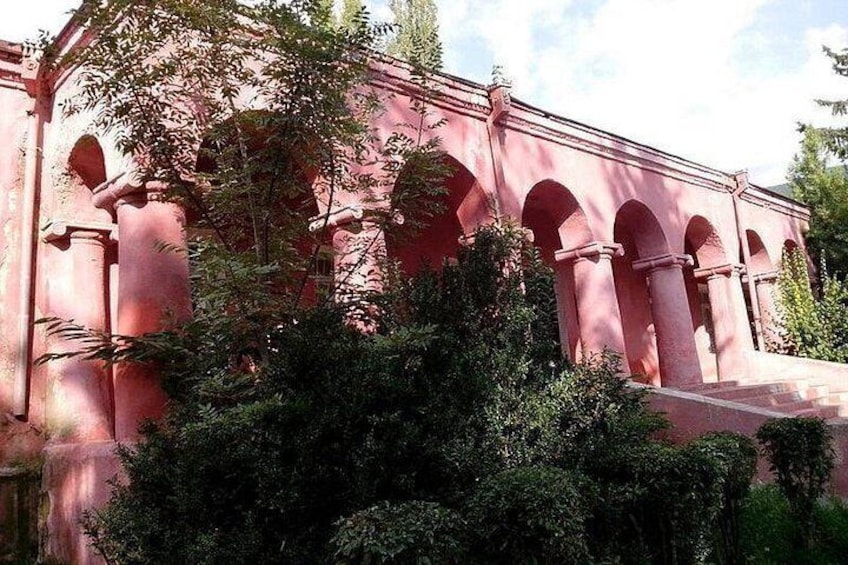 A pink building with arches and columns, surrounded by dense greenery. 3
