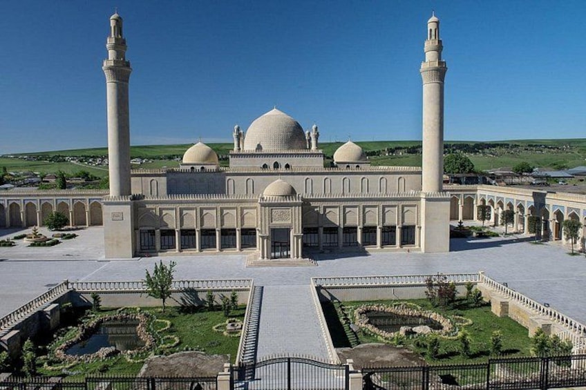 A large mosque with two minarets, a central dome, and a courtyard with geometric garden designs. 3