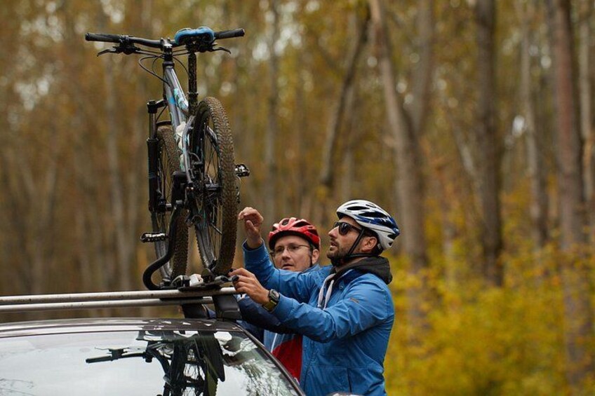 Two people installing a bicycle on a car roof in a forested area. 5