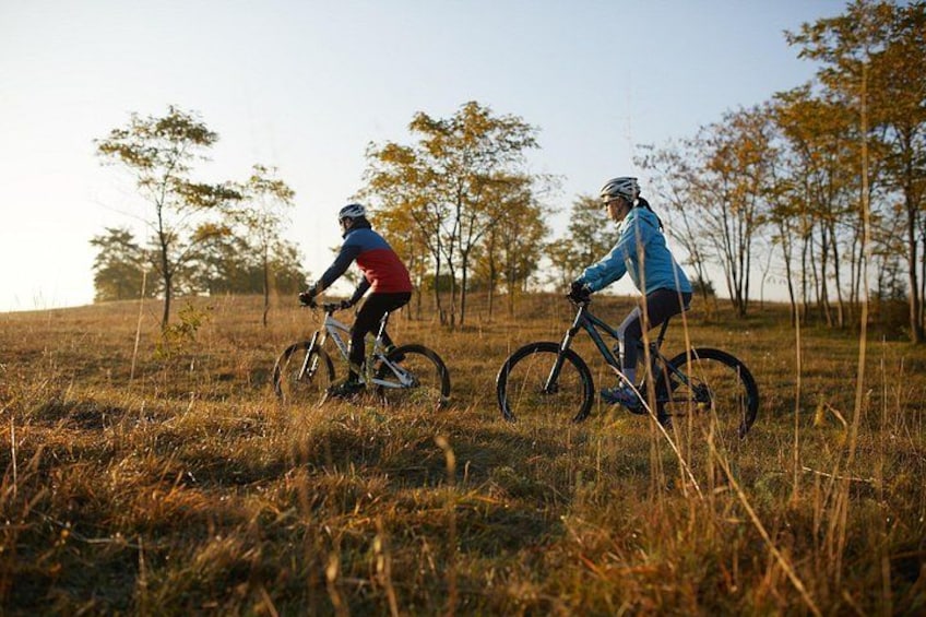 Two cyclists on a trail in a grassy field with trees in the background. 1