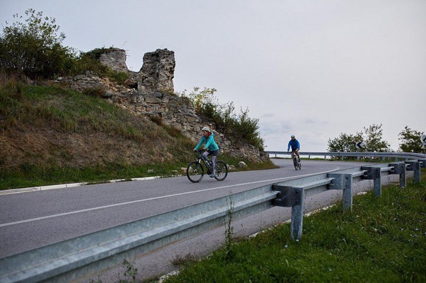Une route asphaltée où l’on voit des cyclistes, une structure en pierre et une barrière de sécurité. 4