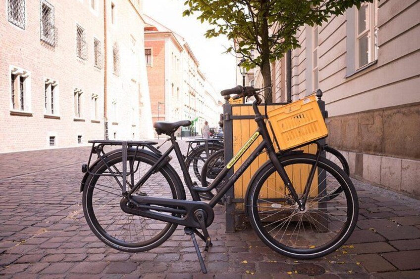 A black bicycle parked on a cobblestone street with a yellow basket attached to the rear. 4