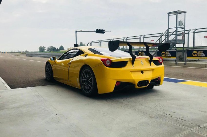 A yellow sports car parked on a concrete surface near a race track. 1