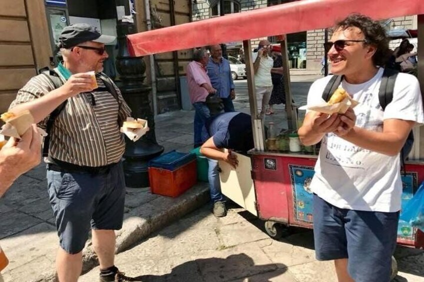 Two men eating food from a street vendor cart. 1