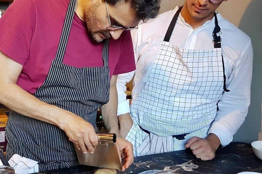 Zwei Personen mit Schürzen, eine schneidet mit einem Messer, die andere schaut zu. 2