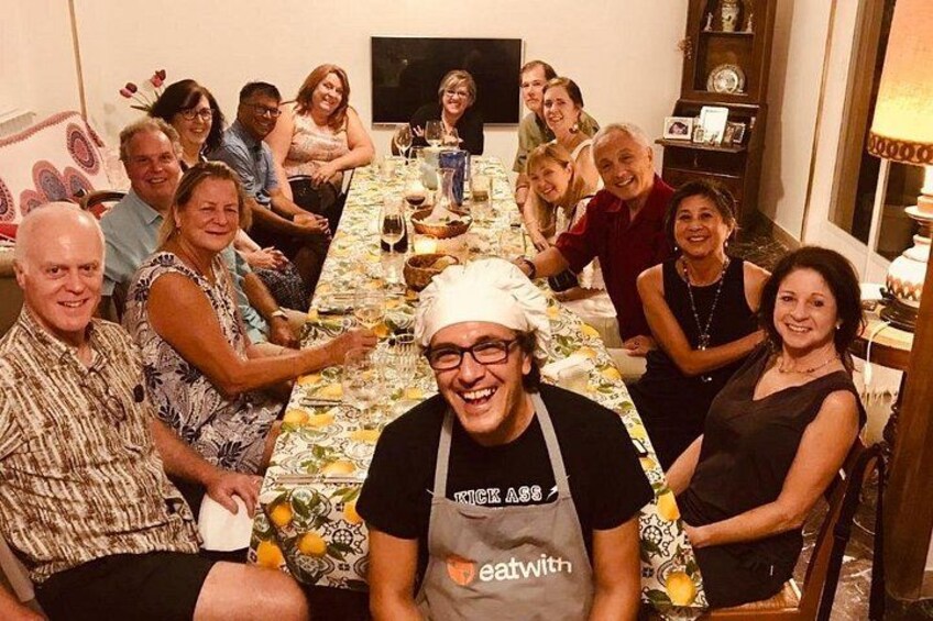 Un grupo de personas sentadas alrededor de una mesa larga cubierta con un mantel floral, conversando. 1