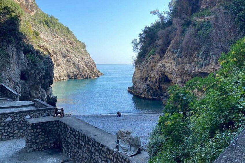 A coastal landscape with a rocky cliff, a stone staircase, and a person sitting on the beach. 2