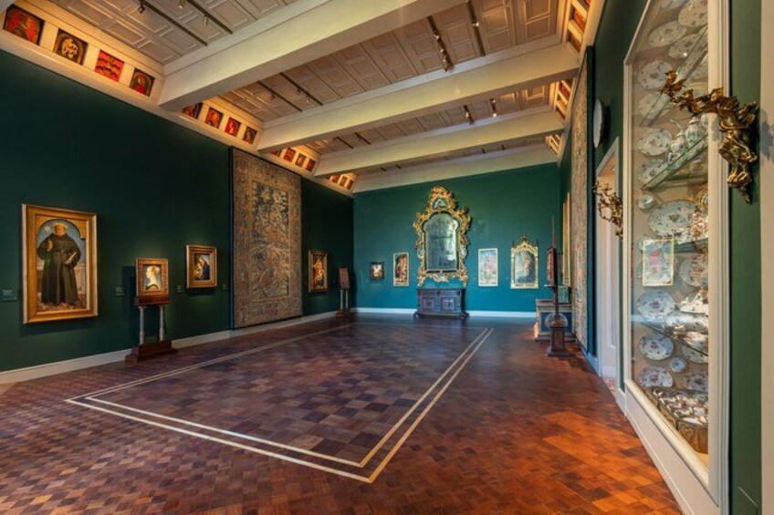 Ett konstgalleri med trägolv, gröna väggar och tavlor i ramar. 1