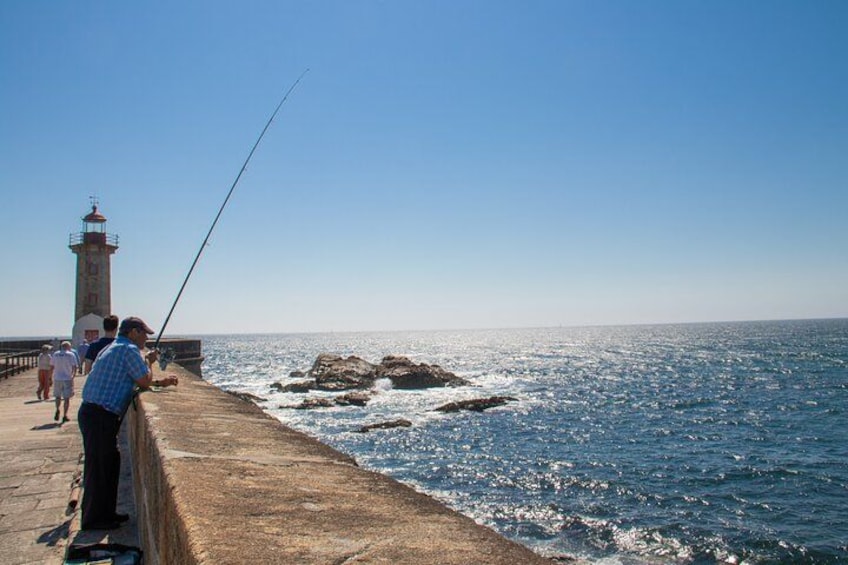 A lighthouse, rocky shoreline, and people fishing by the sea. 2