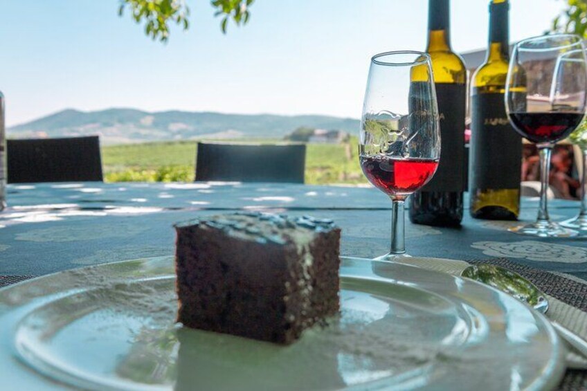 A slice of cake on a plate, two wine glasses, and two wine bottles on a table with a scenic view in the background. 5