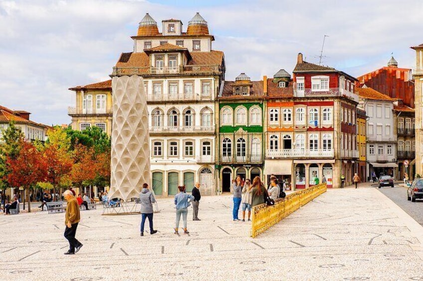 Una plaza histórica con gente caminando, una llamativa escultura moderna y edificios coloridos. 2