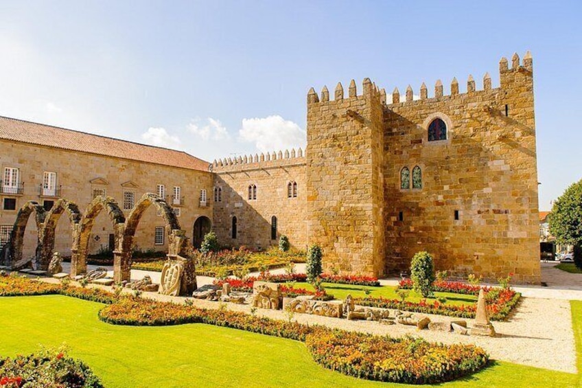 Un edificio histórico de piedra con una torre, rodeado de jardines cuidados y arcos. 2