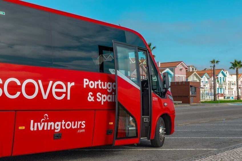 A red bus with 'Portugal & Spain' and 'Living Tours' on the side, parked on a street with houses in the background. 5