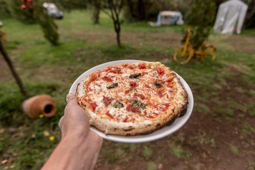 A person holding a pizza outdoors. 2