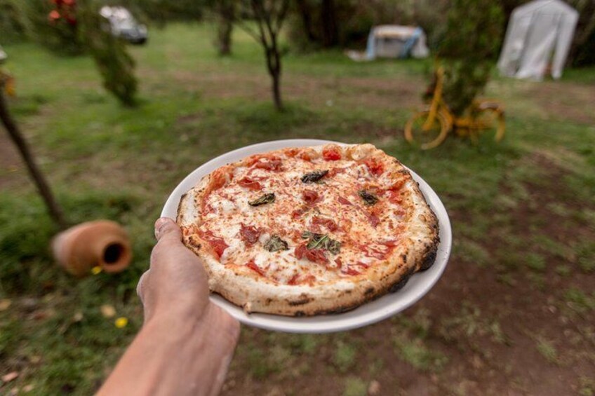 A person holding a pizza outdoors. 2
