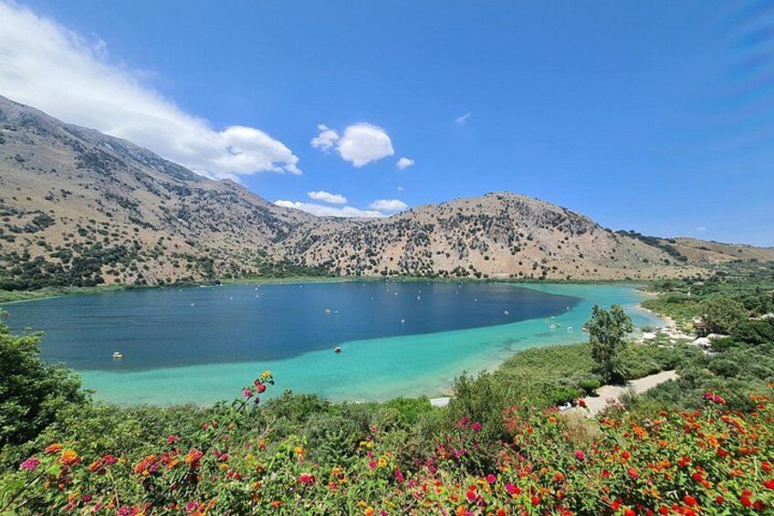 A lake surrounded by mountains, clear blue water, and colorful flowers in the foreground. 1