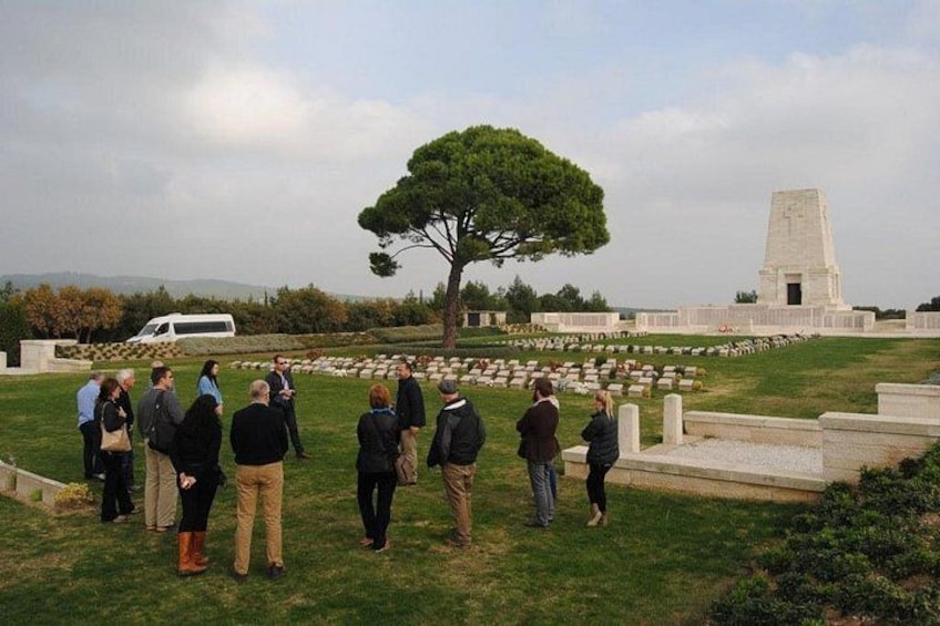En grupp människor som står på en gräsyta, med ett monument och ett träd i bakgrunden. 1