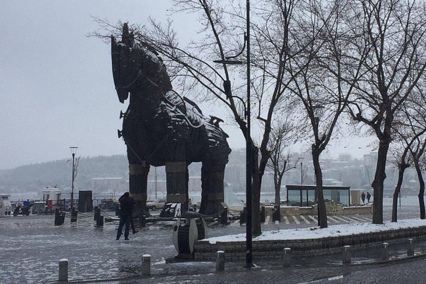 A large horse statue in a snowy park with bare trees and a distant view of a city. 3