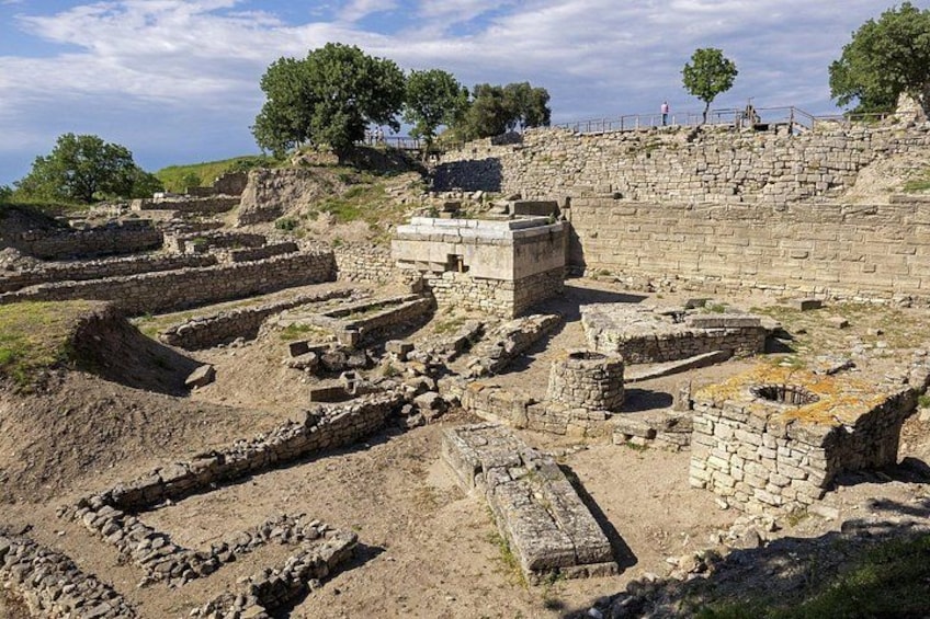 Ancient ruins with stone structures and walls, surrounded by trees and a clear sky. 4