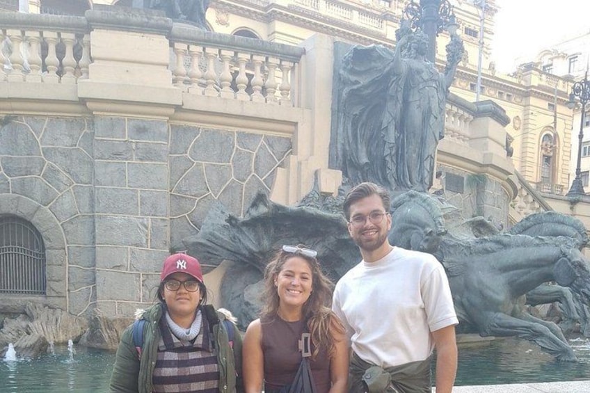 Tres personas de pie frente a una fuente con una estatua al fondo. 2