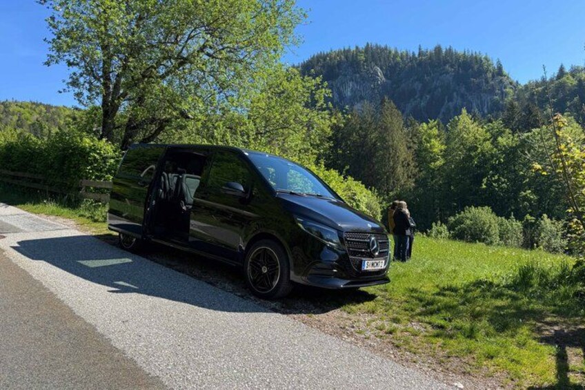 A black van parked on a road with a forested hillside in the background. 2