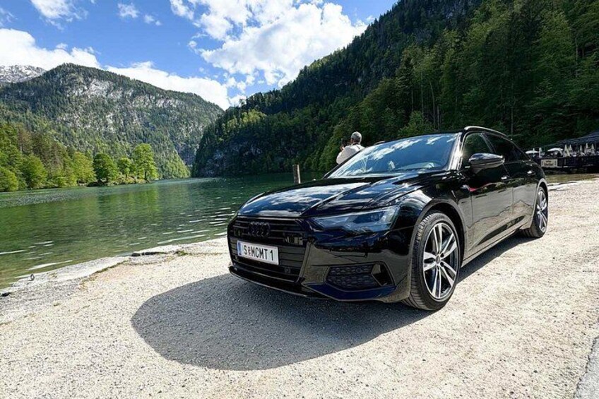 A black car parked by a lake with mountains in the background. 3