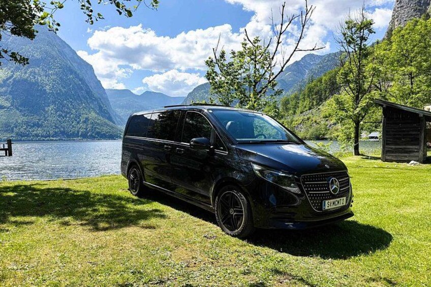 A black van parked on a grassy area near a lake with mountains in the background. 3
