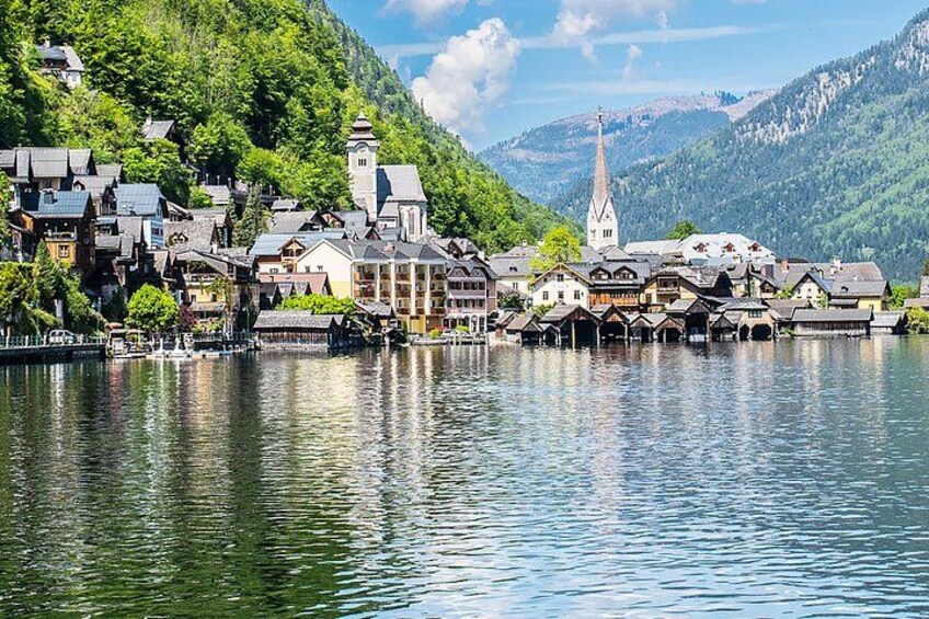 A lakeside town with buildings, a church, and mountains in the background. 2