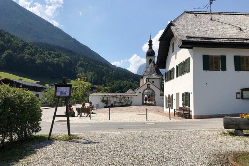 A church with a bell tower, a white building with green shutters, and a mountain in the background. 2